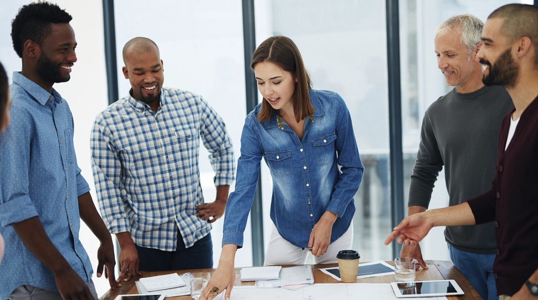 One staff member asks questions about a plan around a table with other staff members